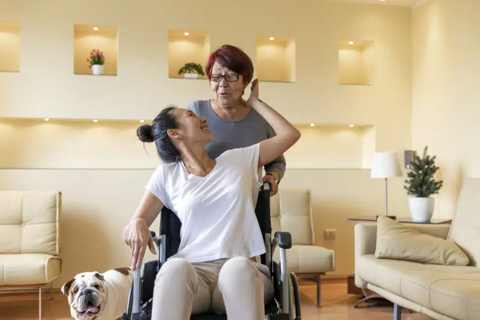 Mature Woman is Happy to Have a Caregiver by her Side. Asian Woman with Physical Disabilities is Glad to Receive Care by an Older Woman.