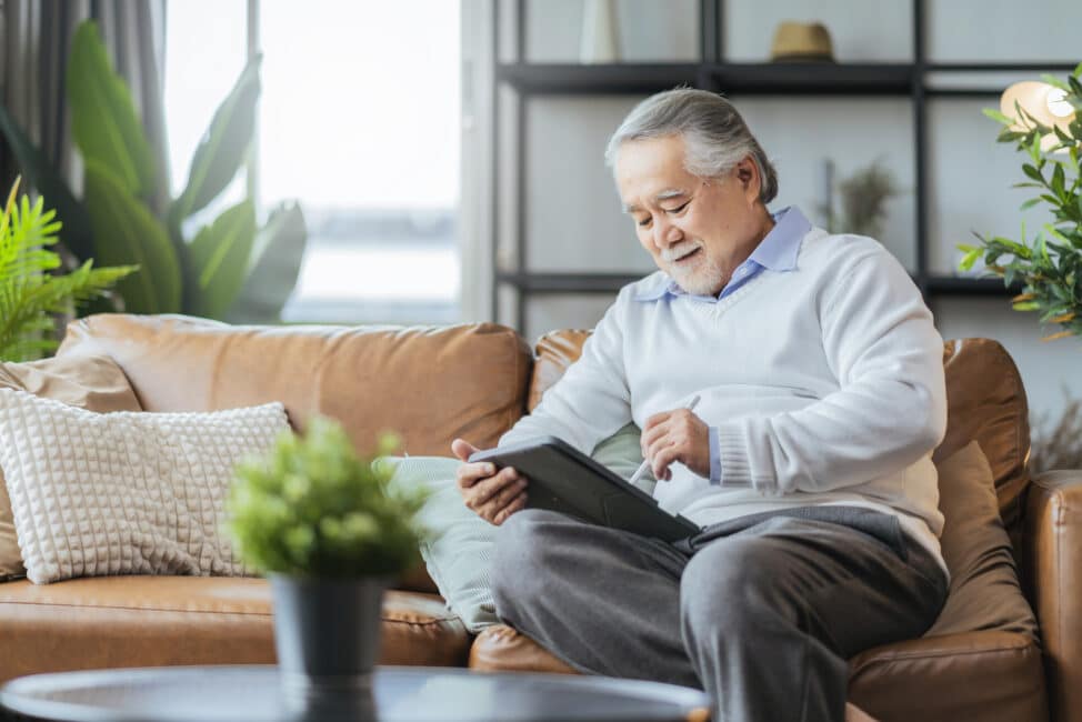 Senior relaxing on couch while using a tablet computer with a stylus
