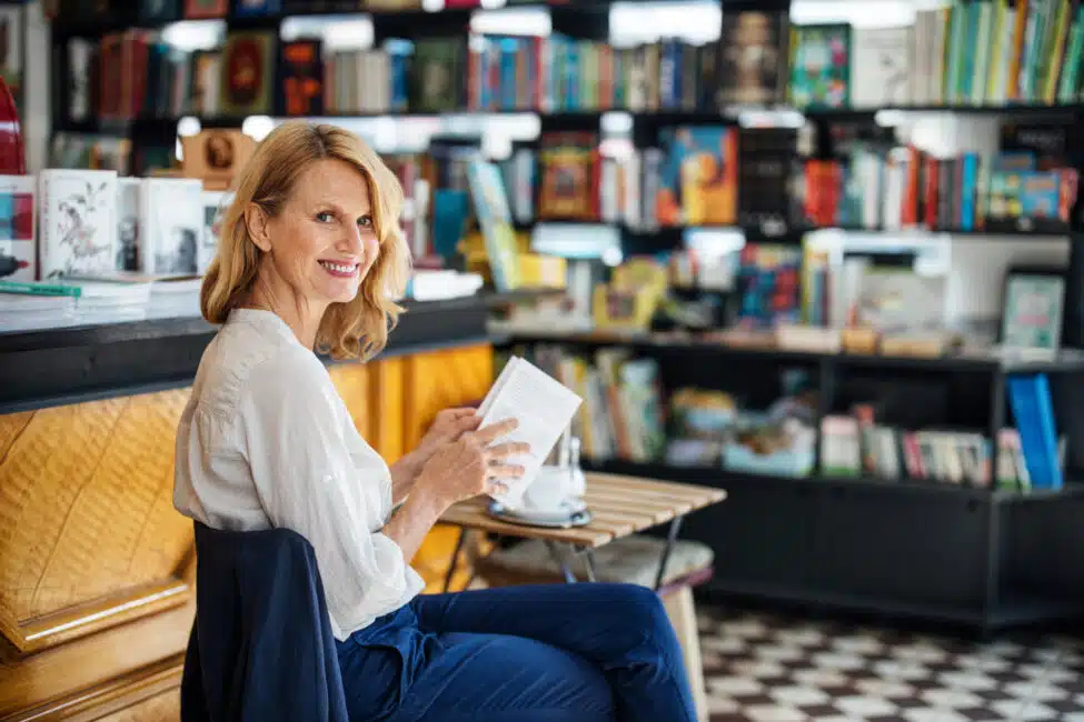 Smiling mature woman sitting in a bookstore cafe with a book. Happy female customer in a bookstore reading a book.